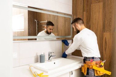 Adam onun yenilenen tuvaletinde duvara bir ayna yükleme.