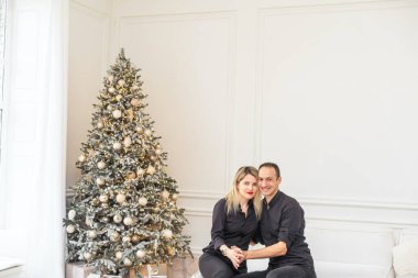 Mutlu Noeller ve mutlu yıllar. Güzel bir çift yeni yılı birlikte beklerken ellerinde hediye kutusuyla güzel bir Noel ağacının yanında kucaklaşıyorlar. Yüksek kalite fotoğraf