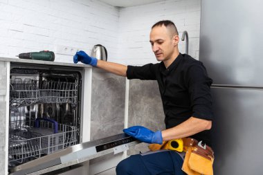 Genç Tamirci, mutfakta tornavidayla bulaşıkçıyı tamir ediyor. Yüksek kalite fotoğraf
