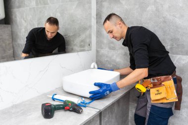 Kireç ve lekeleri temizlemek için banyo lavabosunu kazıyıcı bıçak ve mikro fiber bezle temizleyen bir adam. Yüksek kalite fotoğraf