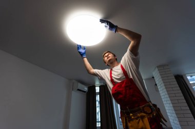 Genç adam mutfaktaki merdivene lamba yerleştiriyor..