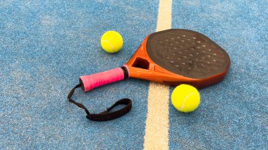 Turuncu bir padel raketi ve mavi bir kortun zemininde bir top. Padel konsepti. Kürek takımı. Yüksek kalite fotoğraf