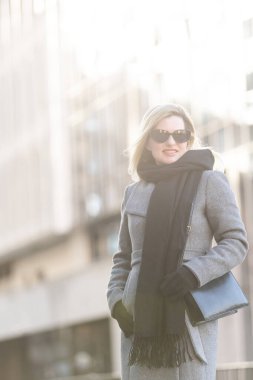 Siyah ceketli, siyah eşarplı genç bayan soğuk sonbahar gününde gün batımında arka planda güneş ışınlarında yürüyor. Yüksek kalite fotoğraf