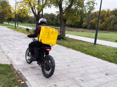 Bir teslimatçı elinde internet siparişiyle caddede motosiklete biniyor. Restorandan ve dükkandan yemek teslimatı. Yüksek kalite fotoğraf