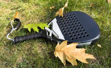 Ağ arkasında yeşil bir kort çimenliği üzerinde siyah bir padel raketinin üst görüntüsü. Kürek bir raket oyunudur. Profesyonel spor konsepti, metin için boşluk. Yüksek kalite fotoğraf