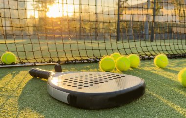 Padel raket ve padel topu gün batımında yeşil bir kortta. Yüksek kalite fotoğraf