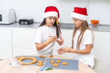 İki kız kardeş Noel kurabiyeleri yaptıktan sonra mutfakta oynuyorlar, masaya ve yüzlerine un çiziyorlar. Noel, yeni yıl konsepti. Yüksek kalite fotoğraf