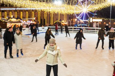 Genç bir kadın Noel arifesinde şehir meydanında buz pateni yapıyor. Kış tatili Yeni yıl büyüsü. Işıklar yansın. Yüksek kalite fotoğraf