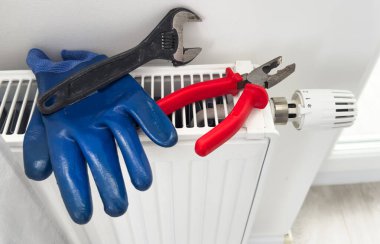 Yeni termostat, ayarlanabilir ingiliz anahtarı ve ısıtma kaloriferinde PTFE bandı. Bir apartmanın ekonomik ısıtması için radyatöre termostat yerleştirmek. Tesisat işi ve servis. Yüksek kalite fotoğraf