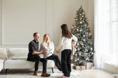 Mutlu Noeller ve mutlu tatiller. Anne, baba ve çocuk hediye değiş tokuşu. Ebeveynler ve kızları kapalı alanda eğleniyorlar. Odada hediyeleri olan sevgi dolu bir aile. Yüksek kalite fotoğraf