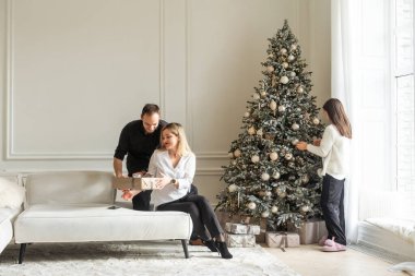 Noel arifesinde çocuklu güzel mutlu bir aile. Neşeli genç ebeveynler ve sevimli küçük kızları Noel ağacının yanında beraberler. Yüksek kalite fotoğraf