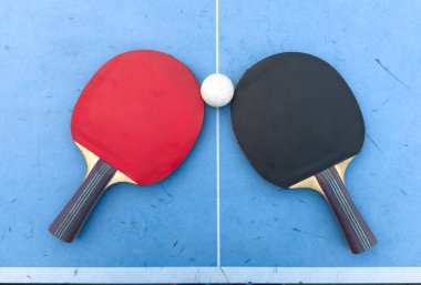 Masa tenisi için kırmızı ve siyah raketler ve mavi arka planda beyaz top. Masa tenisi spor ekipmanları minimum düzeyde. Düz konum, üst görünüm, kopyalama alanı. Yüksek kalite fotoğraf