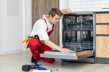 Bulaşık makinelerinin tamiri. Tamirci mutfakta bulaşık makinesini tamir ediyor..