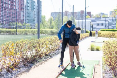 Golf tecrübelerimle paylaşıyorum. Neşeli genç bir adam kızına gündüz vakti mini golf oynamayı öğretiyor. Arkadaş canlısı aile kavramı. Yüksek kalite fotoğraf