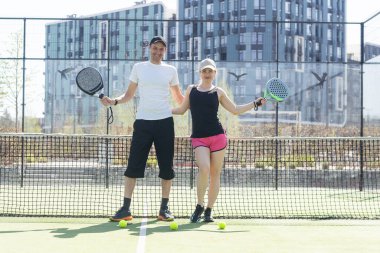 Padel kortunda raketlerle poz veren iki gülümseyen sporcunun portresi. Padel oyuncuları. Yüksek kalite fotoğraf