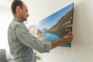 Galeri ambalajı ve kuru çim iç dekorlu tuval baskısı. Kadın fotoğrafçılığı beyaz duvara asıyor. Ellerinde Fransa 'nın Biarritz şehrindeki adanın resmi olan bir tuval var. Yüksek kalite fotoğraf