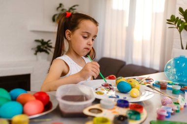 Şirin küçük kız fırçayla yumurta boyuyor. Paskalya konsepti