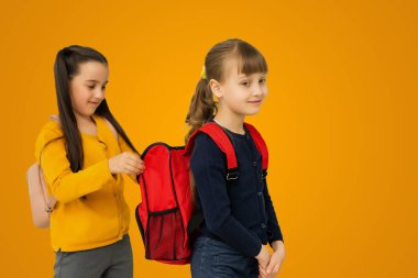 Education Concept. Set portrait of diverse schoolchildren holding stack of academic books and wearing backpack, yellow orange color studio background.