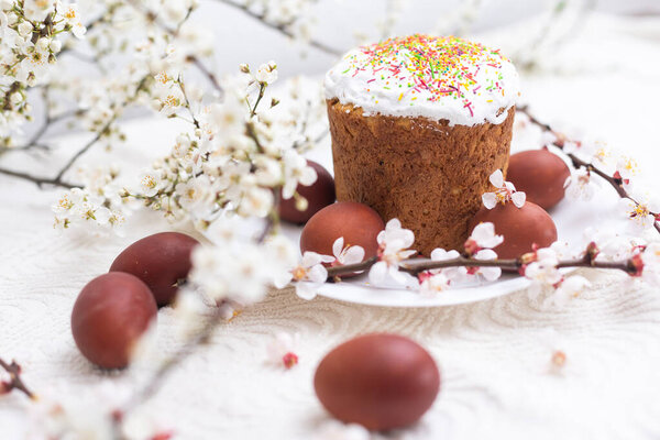 Easter composition. A blooming apricot branch, painted eggs and a glazed Easter cake decorated with sugar sprinkles.
