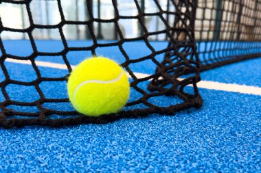 Açık havada mavi kortta kürek ağının arkasında sarı top var. Padel tenisi bir raket oyunudur. Profesyonel spor konsepti. Yüksek kalite fotoğraf