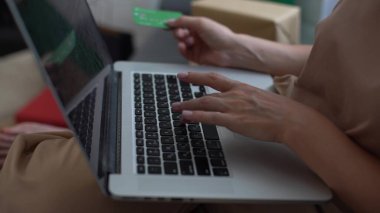 Smiling woman with laptop and credit card at home. Girl with laptop and bank card indoors. Beautiful woman lying in the living room shopping online with credit card. Easy pay using digital gadget