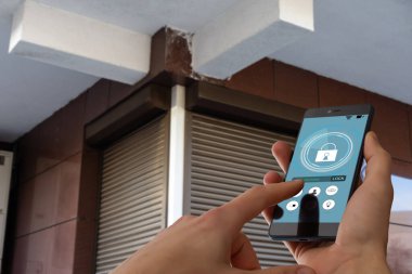 Cep telefonundaki uygulamayı kullanarak içeri girmek ve binadan geçmek için gizli anahtar kodu girerken kesilmiş görüntü, akıllı ev sistemini etkisiz hale getirmek için kontrol panelindeki düğmelere basan kadın.