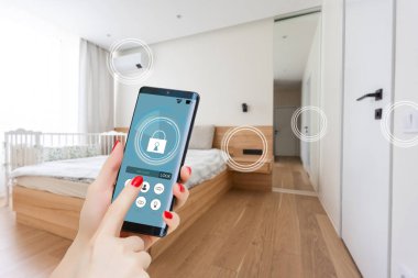 Akıllı ev otomasyon uygulaması arka planda ev içi olan kadın eliyle akıllı telefondan tutulan.