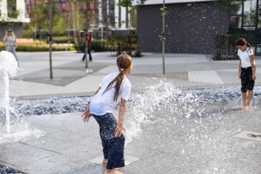 Sıcak bir günde, çocuklar koşar ve şehir çeşmesinde eğlenirler. Boş zaman konsepti. Yaz tatili. Mutlu çocukluk. Yüksek kalite fotoğraf