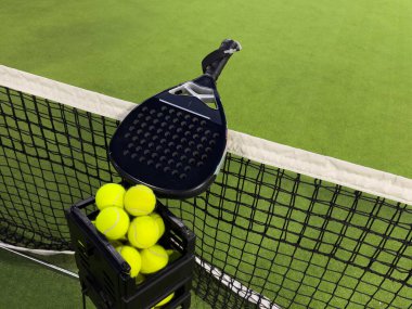 Padel raketi ve sarı top ağların arkasında açık havada çimlerin üzerinde. Kürek bir raket oyunudur. Profesyonel spor konsepti, metin için boşluk. Yüksek kalite fotoğraf