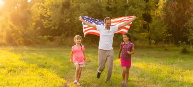 Amerikan bayrağı taşıyan ebeveynler ve çocuklar renkli bir uçurtmayla oynuyorlar. Anne, baba ve küçük kızları sisli bir günde 4 Temmuz 'u birlikte kutluyorlar. ABD 'nin Bağımsızlık Günü konsepti