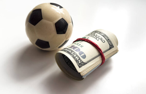 Маленький футбольный мяч с рулоном долларов лежит. Высокое качество фото