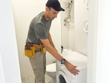 Profesyonel alet çantalı işçi kıyafetli genç yakışıklı tamirci banyodaki çamaşır makinesini tamir ediyor. Yüksek kalite fotoğraf