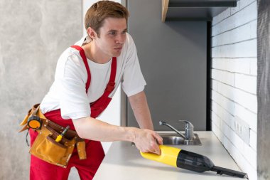 Profesyonel temizlik servisinden bir adam elektrikli süpürgeyle mutfak mobilyalarını temizliyor. Tamirattan sonra odayı hazırla. Temizlik ve ev konsepti