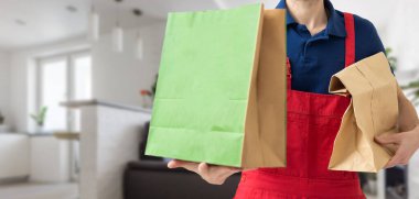 Kağıt cep ve yiyecek kapları gülen bir teslimatçının elinde. - Bir restoranın kaliteli servisi.