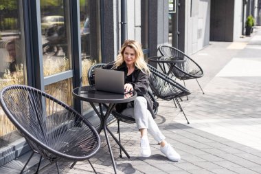 Genç bir kadın açık kafede oturmuş laptopla konuşuyor, bir şeyler anlatıyor, kahve içiyor. Yüksek kalite fotoğraf