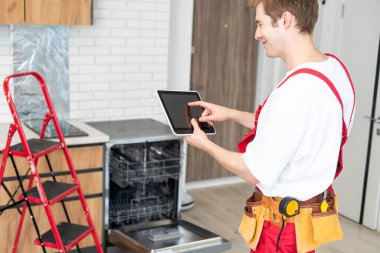 Üniformalı teknisyen ya da işçi mutfak mobilyalarına bulaşık makinesi yerleştiriyor. Tamirci bulaşık makinesini tamir ederken işçi kıyafeti giyer. Koruyucu eldivenlerde uzman Bulaşık makinesini tamir eder.