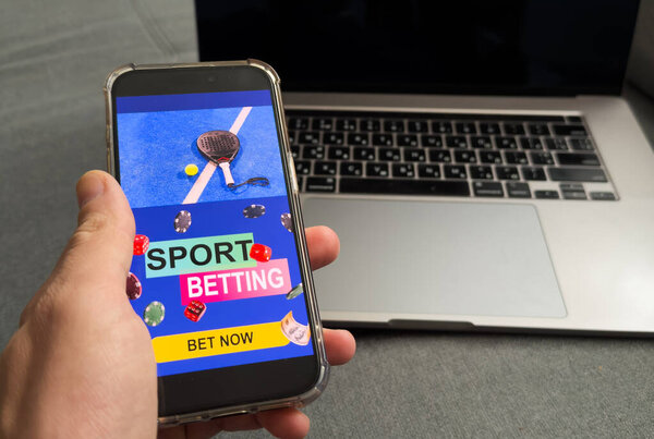 Close up of man holding smartphone with sports bets app to camera while watching football match at home, copy space. High quality photo