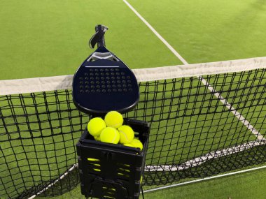 Padel raketi ve sarı top ağların arkasında açık havada çimlerin üzerinde. Kürek bir raket oyunudur. Profesyonel spor konsepti, metin için boşluk. Yüksek kalite fotoğraf