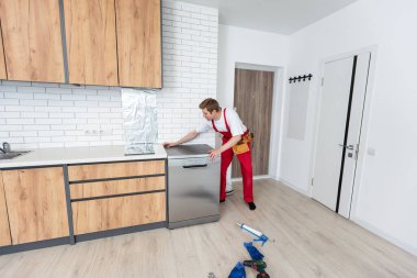 Ev aletlerinin bakım hizmetini kabul et. İşçi bulaşık makinesindeki filtreyi temizler. Erkek tamirci besin kalıntısı filtrelerini kontrol ediyor.