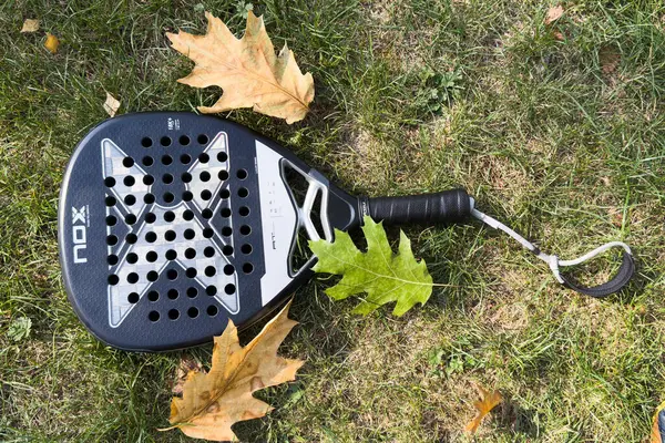 Kyiv, Ukrayna, 29 Eylül 2024, ağların arkasındaki yeşil çimlerin üzerinde siyah padel raket nox. Kürek bir raket oyunudur. Yüksek kalite fotoğraf