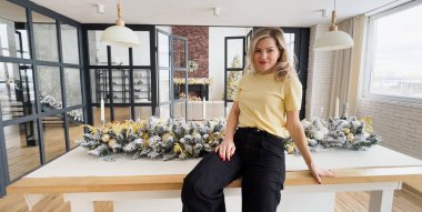 Stüdyoda gülümseyen güzel bir kadın beyaz bir Noel ağacının arka planında parlak bir çelenkle poz veriyor. Yüksek kalite fotoğraf