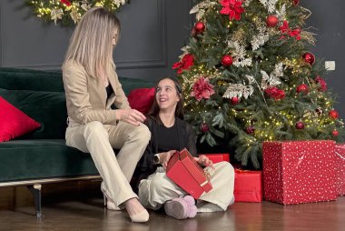 Mutlu aile Noel 'de mutluluğu paylaşır. Anne, sevgili çocuğundan Noel gününde hediyeler alır. Gülümseyen kız, arka planda süslemeli ağaçla birlikte anneye oturma odasında hediye veriyor. Yüksek kalite fotoğraf