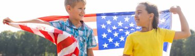 Çocuklar açık havada Amerikan bayrağıyla oturuyorlar.