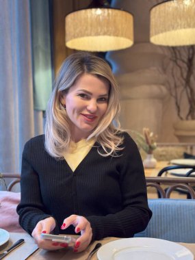 Kafede kahve içen güzel, gülümseyen bir kadın. Kafeteryada sıcak kapuçino içip kameraya bakan olgun bir kadının portresi. Kahveli güzel bir kadın. Yüksek kalite fotoğraf