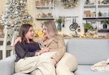 Mutlu aile Noel 'de mutluluğu paylaşır. Anne, sevgili çocuğundan Noel gününde hediyeler alır. Gülümseyen kız, arka planda süslemeli ağaçla birlikte anneye oturma odasında hediye veriyor. Yüksek kalite fotoğraf