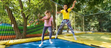 Güzel kızlar parktaki renkli trambolinde birlikte zıplıyorlar. Aktif gösteriler sırasında eğlenen iki kız kardeş. Yüksek kalite fotoğraf