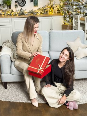 Mutlu aile Noel 'de mutluluğu paylaşır. Anne, sevgili çocuğundan Noel gününde hediyeler alır. Gülümseyen kız, arka planda süslemeli ağaçla birlikte anneye oturma odasında hediye veriyor. Yüksek kalite fotoğraf