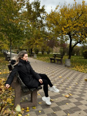 Sonbahar parkında güzel sarışın bir kız, sarı ve turuncu yapraklı siyah bir ceket. Yüksek kalite fotoğraf