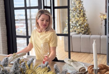 Stüdyoda gülümseyen güzel bir kadın beyaz bir Noel ağacının arka planında parlak bir çelenkle poz veriyor. Yüksek kalite fotoğraf