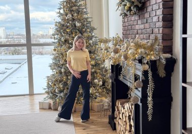 Stüdyoda gülümseyen güzel bir kadın beyaz bir Noel ağacının arka planında parlak bir çelenkle poz veriyor. Yüksek kalite fotoğraf